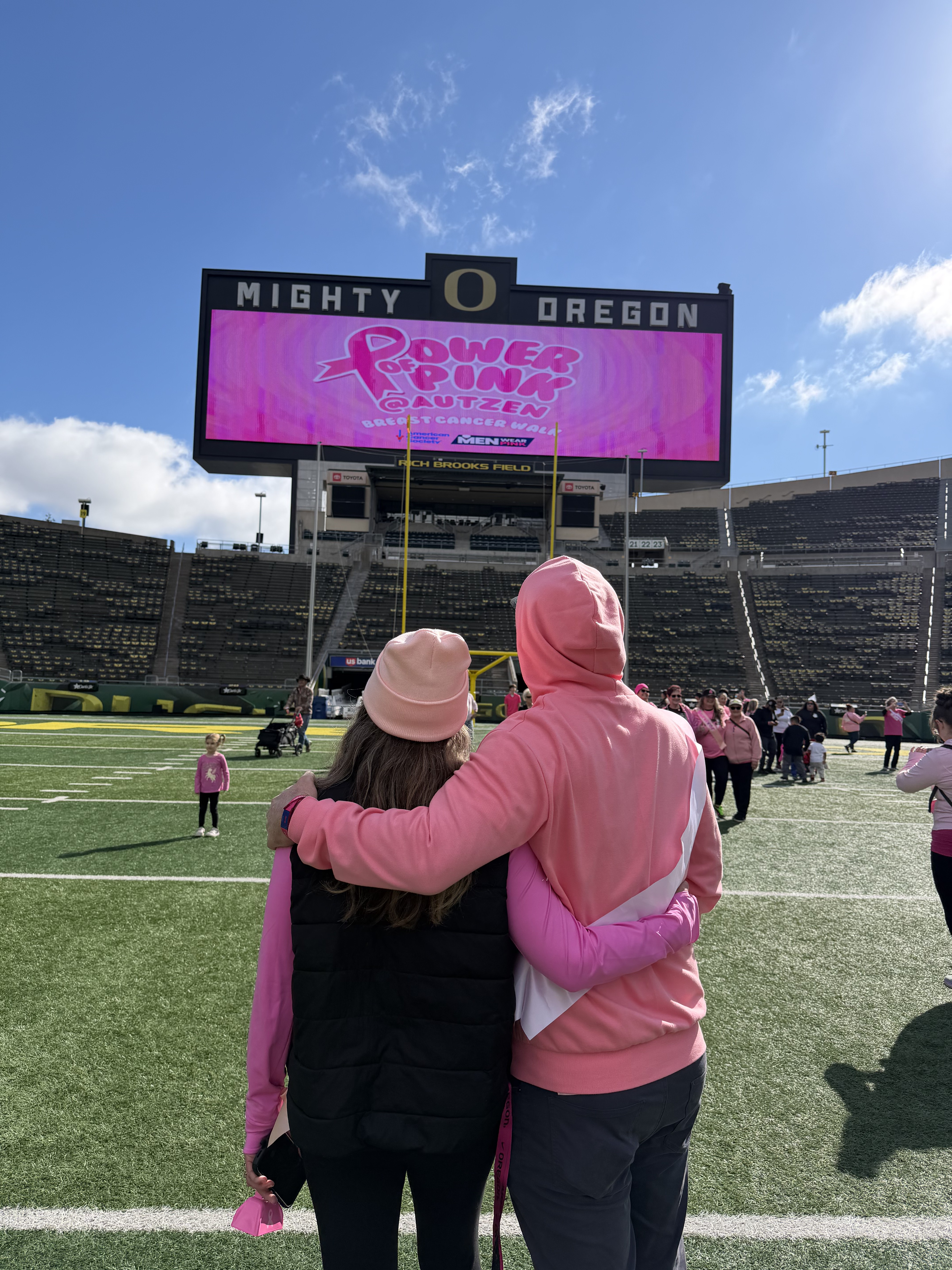 Two supporters embracing on the field at Autzen Stadium during the Power of Pink walk